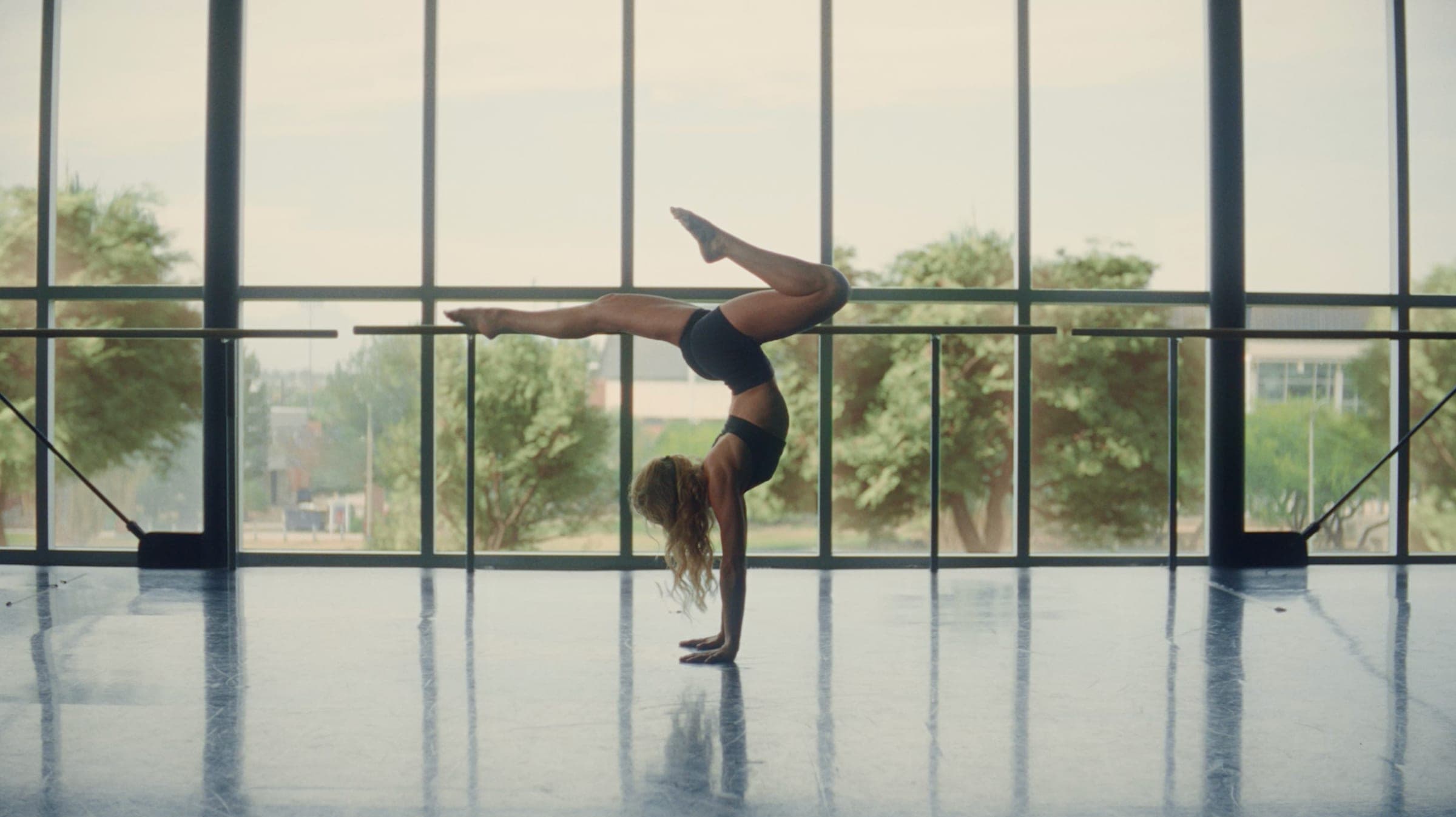 A dancer holding a handstand at the barre of a sunlit studio