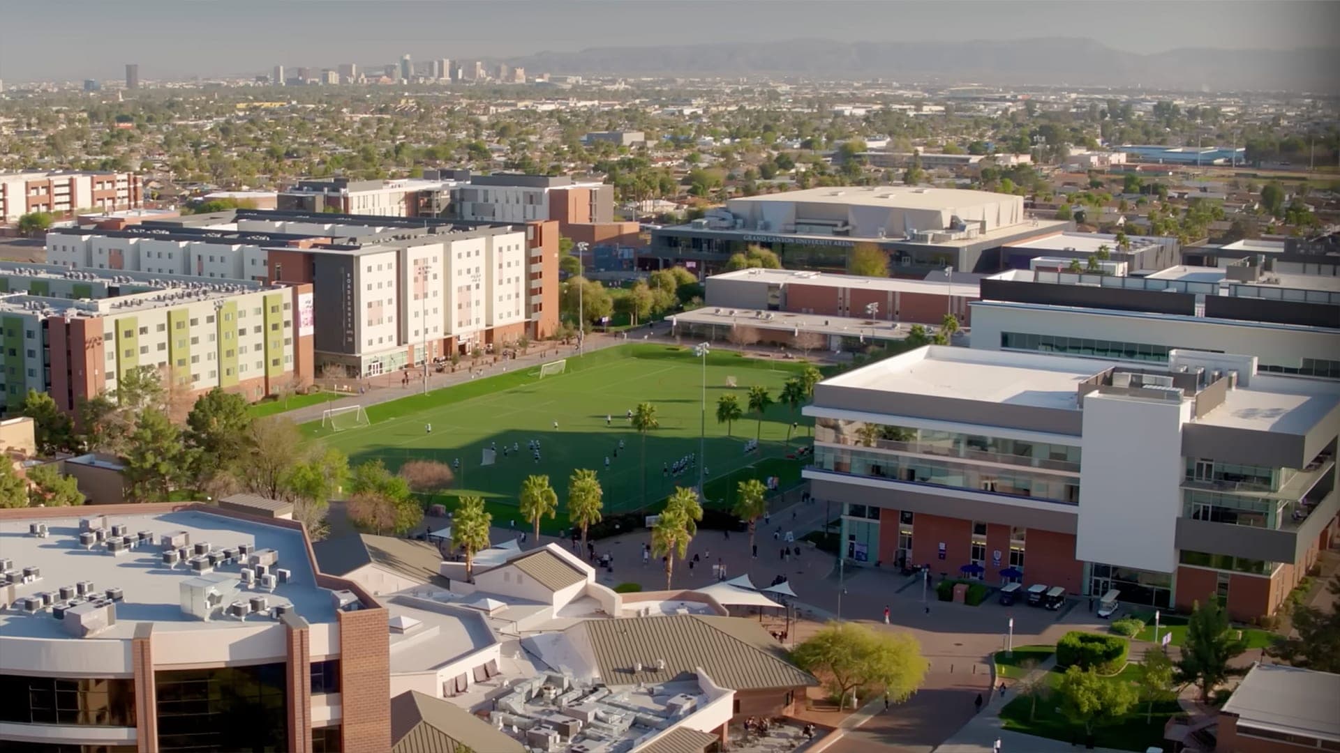 An aerial pass over a university campus with a city skyline beyond