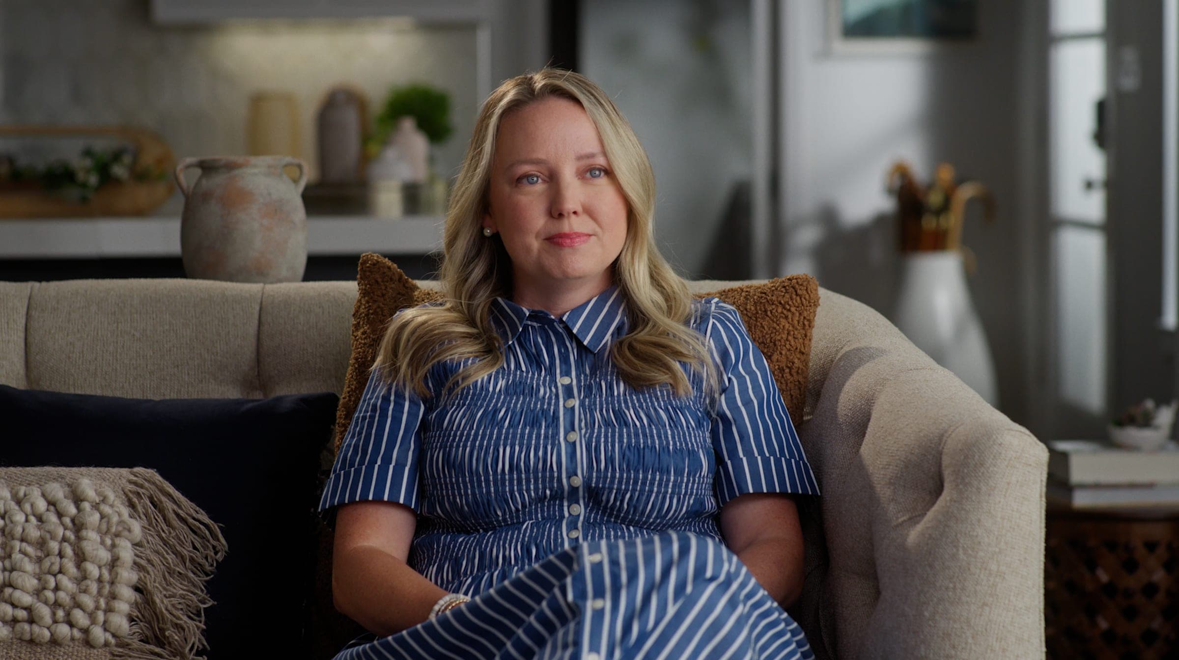 A woman speaking to camera from a sofa in a sunlit living room